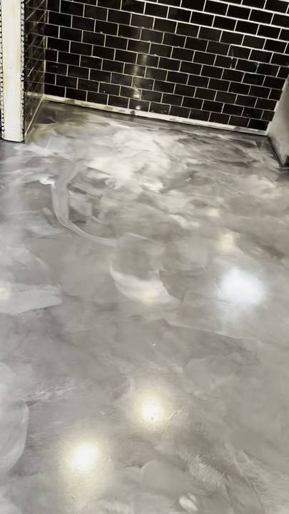 Metallic epoxy floor beside a black subway-tile wall