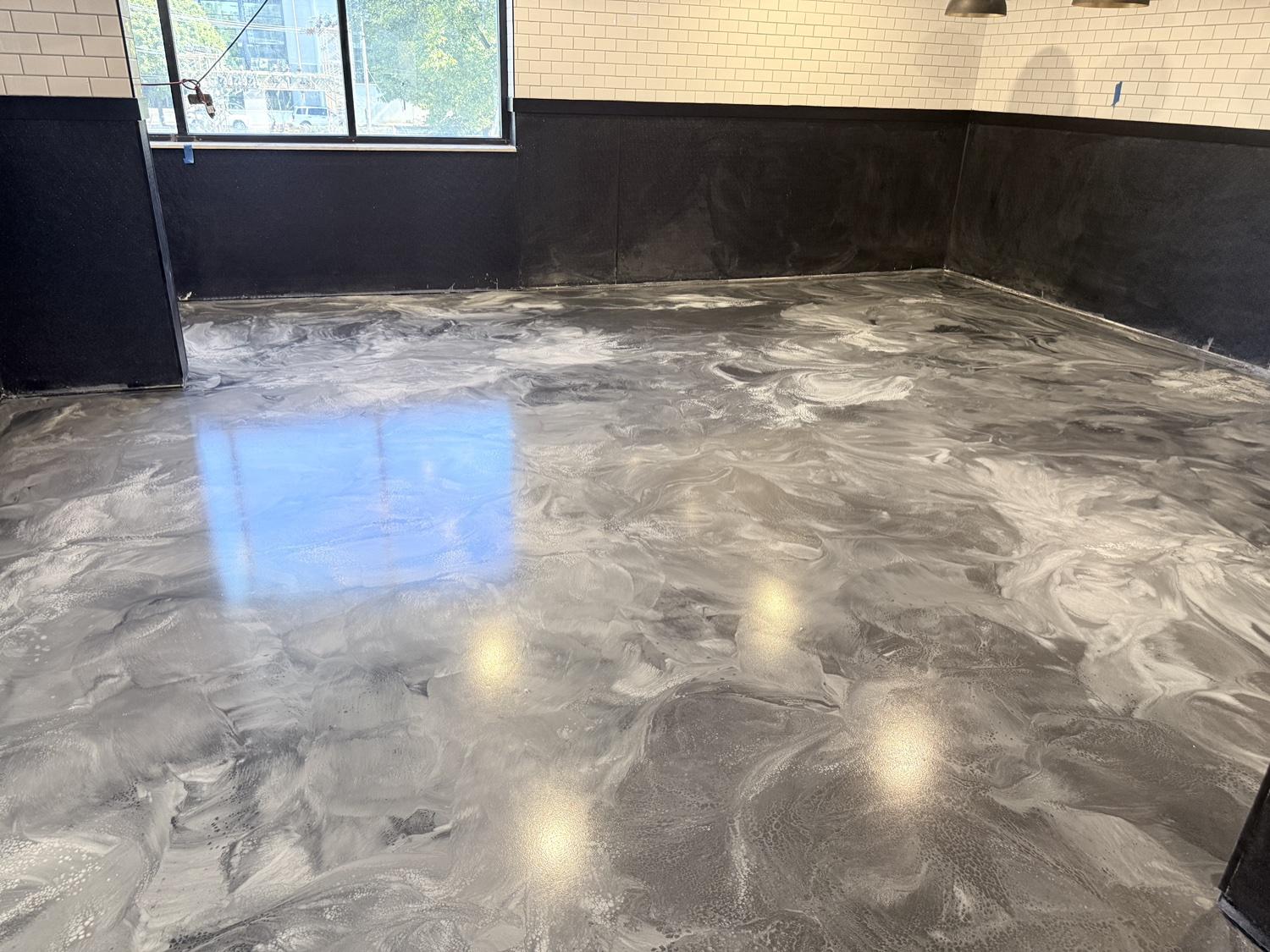 Wide view of a silver and charcoal metallic epoxy floor with a mirror-gloss finish reflecting the windows